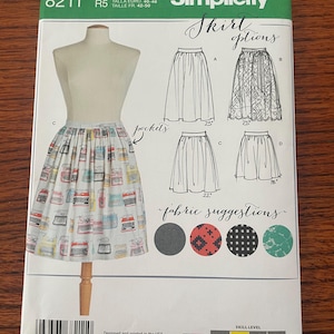 Könnte beinhalten: Ein Simplicity 8211 Schnittmusterumschlag für einen Rock mit Taschen. Die Vorderseite zeigt eine Schneiderpuppe mit einem Rock mit Vintage-Schreibmaschinenmuster. Es enthält Abbildungen für vier Rockstile mit Längen von 38, 56 und 64 cm.