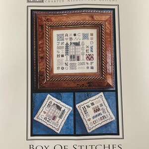 May include: A framed cross-stitch sampler with a house design, surrounded by alphabet letters and other patterns. Below, two smaller cross-stitch pieces are displayed, one with a house and the other with the word "SCISSORS". The text "BOX OF STITCHES" is at the bottom.