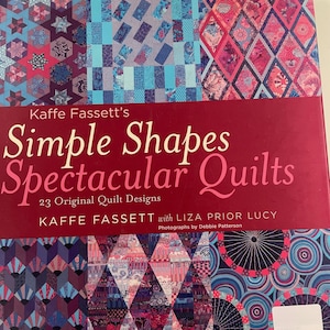 May include: A book titled "Kaffe Fassett's Simple Shapes Spectacular Quilts" with 23 original quilt designs. The cover features colorful quilt patterns in shades of blue, pink, and purple. The author's name is Kaffe Fassett.