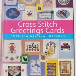 May include: A book titled "Cross Stitch Greetings Cards" with various cross-stitch designs. The cover features a pink and blue banner with the title and the text "OVER 130 ORIGINAL DESIGNS". The book showcases multiple cross-stitch greeting card examples.