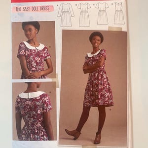 Op de afbeelding: Een Simplicity S8946 R5 naaipatroon-envelop voor The Baby Doll Dress. De verpakking bevat illustraties van vier jurkvariaties en foto's van een jurk met bloemenprint, een witte Peter Pan-kraag en korte mouwen.