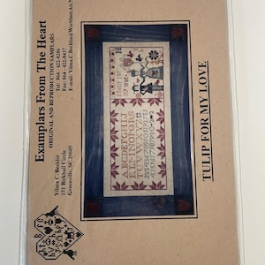 Puede incluir: Un patrón de bordado de punto de cruz titulado "Tulip For My Love" en una funda de plástico. El diseño presenta un panel rectangular central con filas de alfabeto y números, y un borde decorativo. El texto "Examplars From The Heart" es visible.