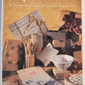 May include: The cover of a book titled "Papercrafts" with the subtitle "50 Extraordinary Gifts & Projects, Step by Step." The image features various papercraft projects, including gift boxes, bows, and decorative items, showcasing the art of paper crafting.