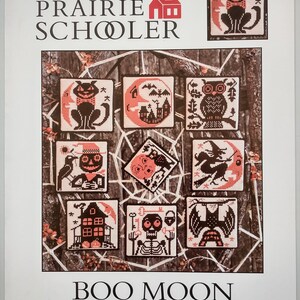 Pode incluir: Capa do livro "The Prairie Schooler" com o título "Boo Moon". Apresenta padrões de ponto cruz com desenhos de Halloween, como um gato preto, uma coruja, uma bruxa e uma casa assombrada, cada um em uma moldura quadrada.