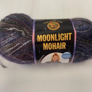 May include: A ball of Lion Brand Moonlight Mohair yarn. The yarn is a mix of purple, blue, and silver, with a soft, fuzzy texture. The label reads "Moonlight Mohair" and features a picture of a woman.