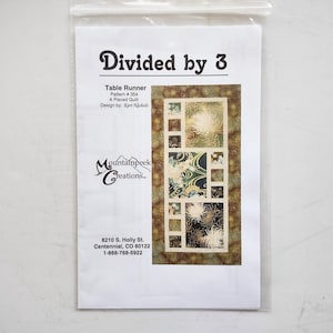 May include: A sewing pattern titled Divided by 3 Table Runner Pattern #354 by Mountainpeek Creations. The cover features a rectangular pieced quilt design with cream, brown, and dark green floral and wave patterns in a grid-like arrangement.