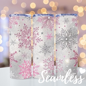 May include: Three stainless steel insulated tumblers with a winter theme. The tumblers feature a white glitter background with pink and silver snowflakes and stars. The word "Seamless" is written in white script on the bottom.
