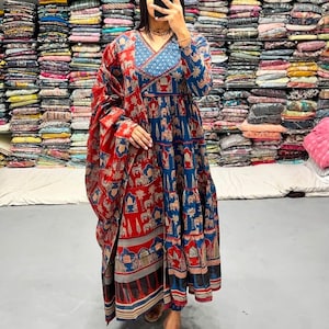 May include: A long, flowing dress and shawl set in blue and red. The dress has a V-neck and a detailed pattern of figures and animals. The shawl drapes over the shoulders, complementing the dress's design. The outfit is suitable for special occasions or cultural events.