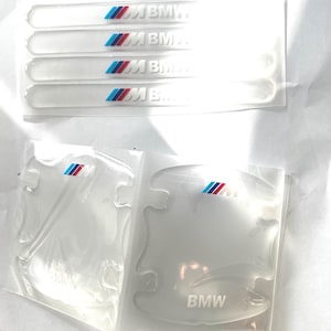 Puede incluir: Juego de láminas protectoras transparentes para vehículos BMW. El juego incluye cuatro tiras largas y rectangulares con el logotipo de BMW y rayas tricolores, y dos protectores de manija de puerta con el logotipo de BMW.