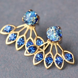 Puede incluir: Pendientes de oro con un diseño en forma de abanico adornado con brillantes azules. Los pendientes tienen un solo brillante azul más grande en la parte superior.