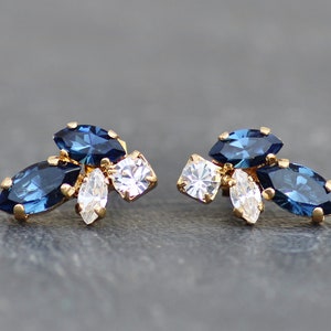 May include: A pair of gold earrings with blue and clear marquise-shaped crystals.