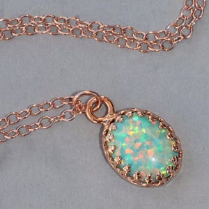 May include: A delicate rose gold chain necklace with a pendant featuring a light green opal stone set in a rose gold filigree frame.