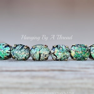 May include: A bracelet with green and gold iridescent glass beads set in brass settings. The bracelet is on a wooden surface. Hanging By A Thread.