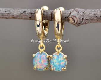 May include: Gold hoop earrings with a dangling opal gemstone. The opal is a light blue color with pink and white flecks.