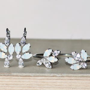 May include: A set of silver jewelry with white opal stones. The set includes a pair of earrings and a bracelet. The earrings and bracelet are designed with a floral motif.