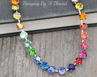 May include: A rainbow crystal necklace with silver chain and round, faceted crystals. The necklace is laid out on a dark gray surface.