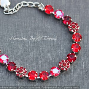 May include: A silver-toned bracelet featuring a series of vibrant red gemstones. The bracelet includes round and flower-shaped stones, connected by a delicate chain. The text "Hanging By A Thread" is visible.