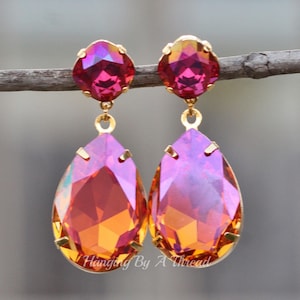 May include: A pair of gold dangle earrings with teardrop-shaped crystals. The crystals are iridescent and have a pink, orange, and yellow colour gradient.