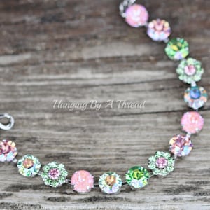 May include: A bracelet made with green, pink, and clear crystal beads. The beads are arranged in a repeating pattern of a single round bead, a flower-shaped bead, and another round bead. The bracelet has a silver clasp.