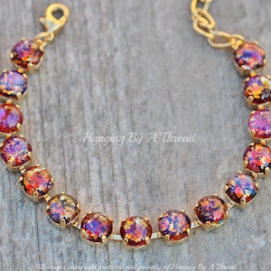 May include: A gold chain bracelet with a row of iridescent opal-like stones. The stones are a mix of red, orange, and purple.