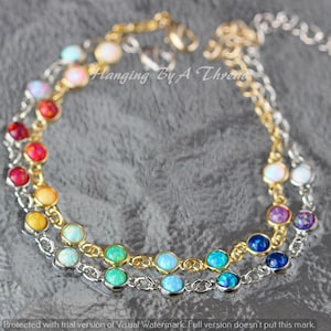 May include: Three delicate bracelets with colorful opal stones. The bracelets are made of gold and silver chains. The opal stones are in various colors, including red, yellow, green, blue, and purple. The text "Hanging By A Thread" is visible.
