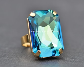 Peut inclure: Une bague en or avec une grande pierre précieuse rectangulaire bleue et verte. La pierre précieuse est facetée et a un grand éclat.