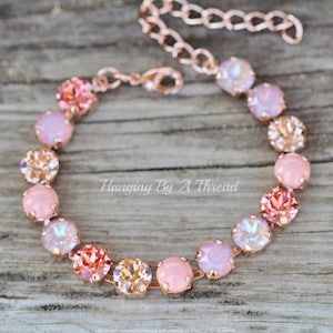 May include: A rose gold bracelet with a graduated ombre design featuring pink, peach, and champagne colored crystals. The bracelet is made with a delicate chain and a lobster clasp.
