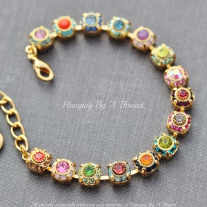 Könnte beinhalten: Ein goldenes Armband mit einem Regenbogen aus bunten runden Steinen. Das Armband besteht aus kleinen, runden Steinen, die in Goldmetall gefasst sind. Die Steine sind in einem Regenbogenmuster angeordnet, mit roten, orangefarbenen, gelben, grünen, blauen, indigofarbenen und violetten Steinen. Das Armband ist ein wunderschönes und einzigartiges Schmuckstück.