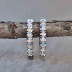 May include: A pair of silver hoop earrings with a row of white opal stones around the edge.