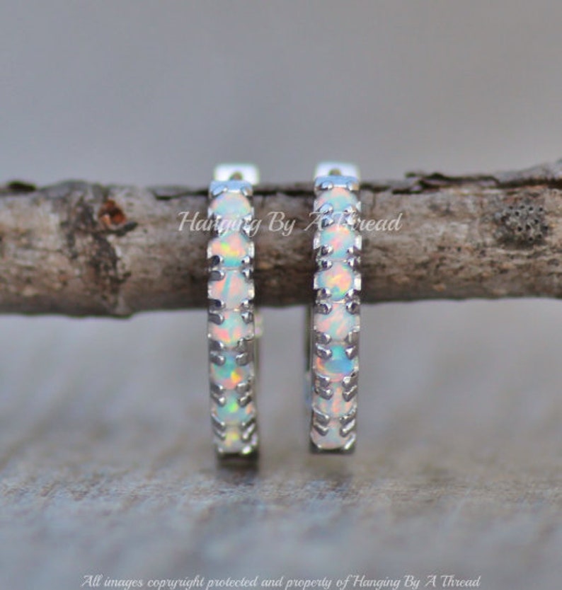 May include: A pair of silver hoop earrings with a row of white opal stones around the edge.