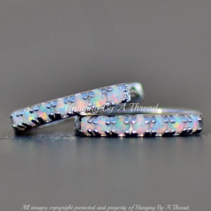 May include: Two silver hoop earrings with a row of small white opal stones set in a black metal bezel.