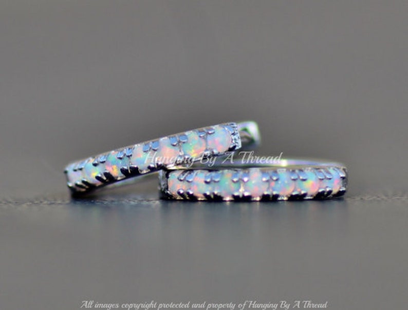 May include: Two silver hoop earrings with a row of small white opal stones set in a black metal bezel.