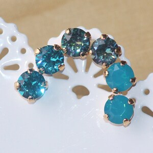 May include: A set of six turquoise and teal blue rhinestones with gold settings. The rhinestones are arranged in a curved shape.