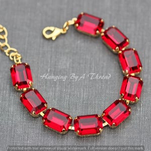 May include: A gold-toned bracelet featuring rectangular, ruby-red gemstones. The bracelet is connected by gold links and has a lobster clasp closure. The text "Hanging By A Thread" is visible in the image.