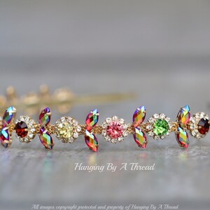 May include: A gold headband with a row of colorful iridescent crystals and small clear rhinestones. The crystals are in a leaf shape and are arranged in a repeating pattern.