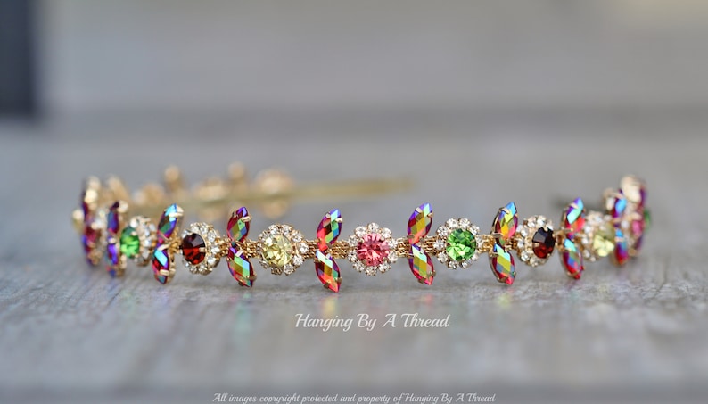 May include: A gold headband with a row of colorful iridescent crystals and small clear rhinestones. The crystals are in a leaf shape and are arranged in a repeating pattern.