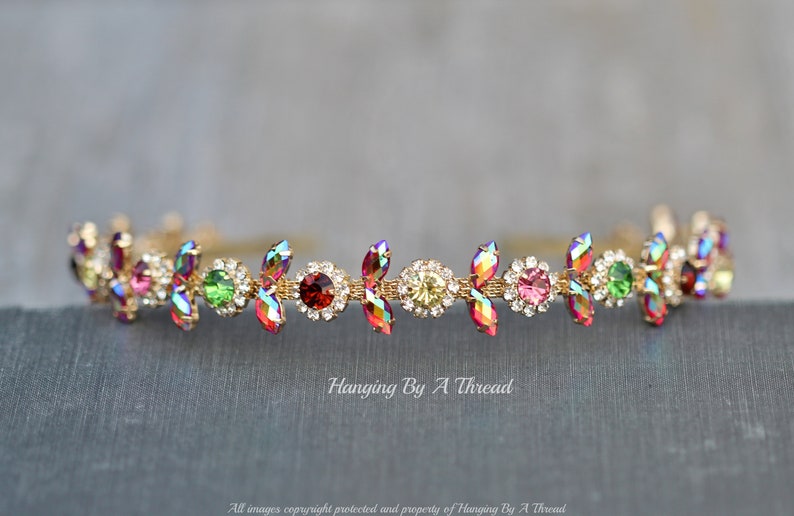 May include: A gold headband with iridescent red, green, and clear rhinestones. The headband is decorated with small, gold leaves.