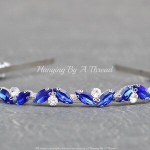 Pu&ograve; includere: Un cerchietto argentato con una fila di strass blu e trasparenti. Il cerchietto &egrave; decorato con un motivo ripetitivo di strass a forma di marquise.