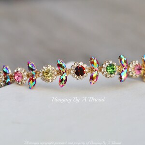 May include: A gold headband with a row of iridescent, multi-colored crystals in a floral design. The crystals are set in a gold metal frame and are arranged in a repeating pattern. The headband is a delicate and elegant accessory.