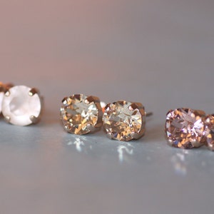 Puede incluir: Tres pares de pendientes de botón de oro con piedras transparentes, marrón claro y rosa.
