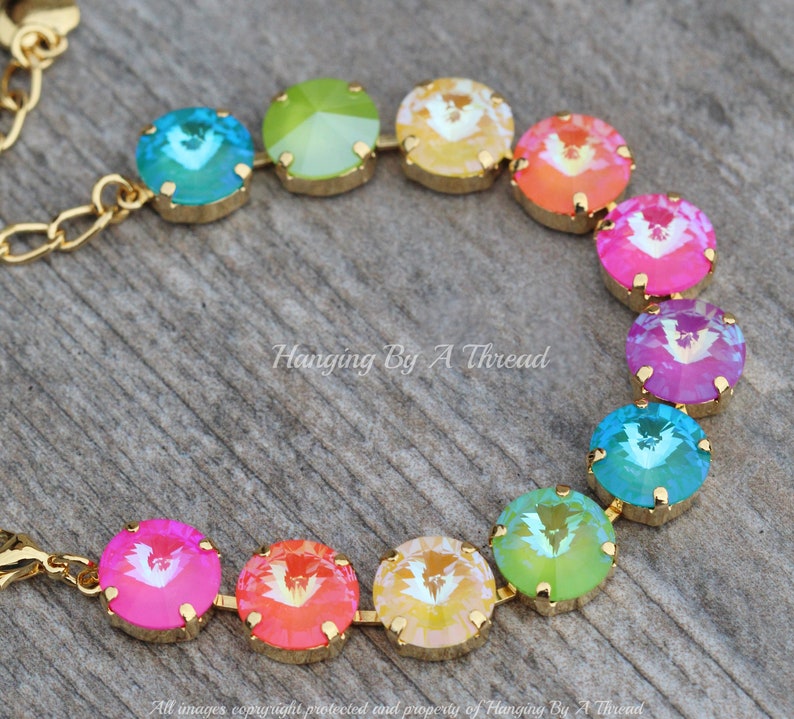 May include: A gold chain bracelet with round, faceted, rainbow-colored crystals. The crystals are arranged in a rainbow pattern, starting with green and ending with pink.