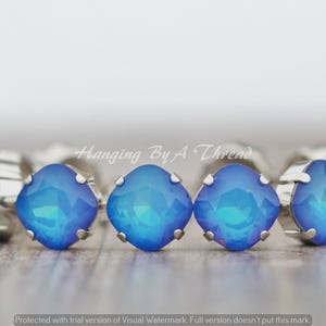 Pode incluir: Um bracelete feito de metal prateado com uma fila de pedras de cristal quadradas azuis iridescentes.