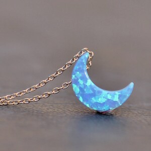 Op de afbeelding: Een delicate gouden ketting met een halve maan hanger gemaakt van blauwe opaal. De opaal heeft een glinsterend, iriserend effect.