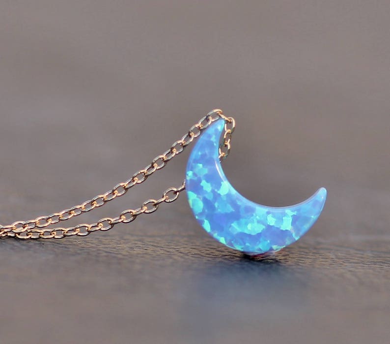 Op de afbeelding: Een delicate gouden ketting met een halve maan hanger gemaakt van blauwe opaal. De opaal heeft een glinsterend, iriserend effect.