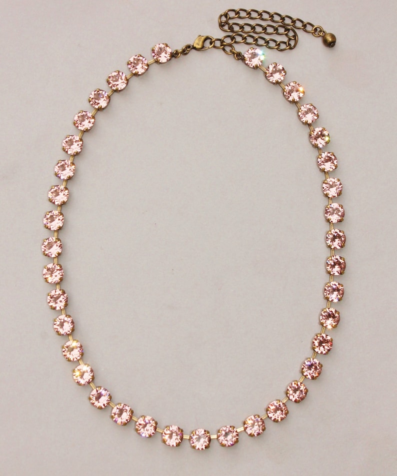 May include: A delicate pink crystal necklace with a gold chain and clasp. The necklace is made of small, round crystals that are strung together in a continuous line.