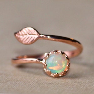 May include: A delicate rose gold ring with a small opal gemstone and a leaf design. The ring is a simple and elegant piece of jewelry.