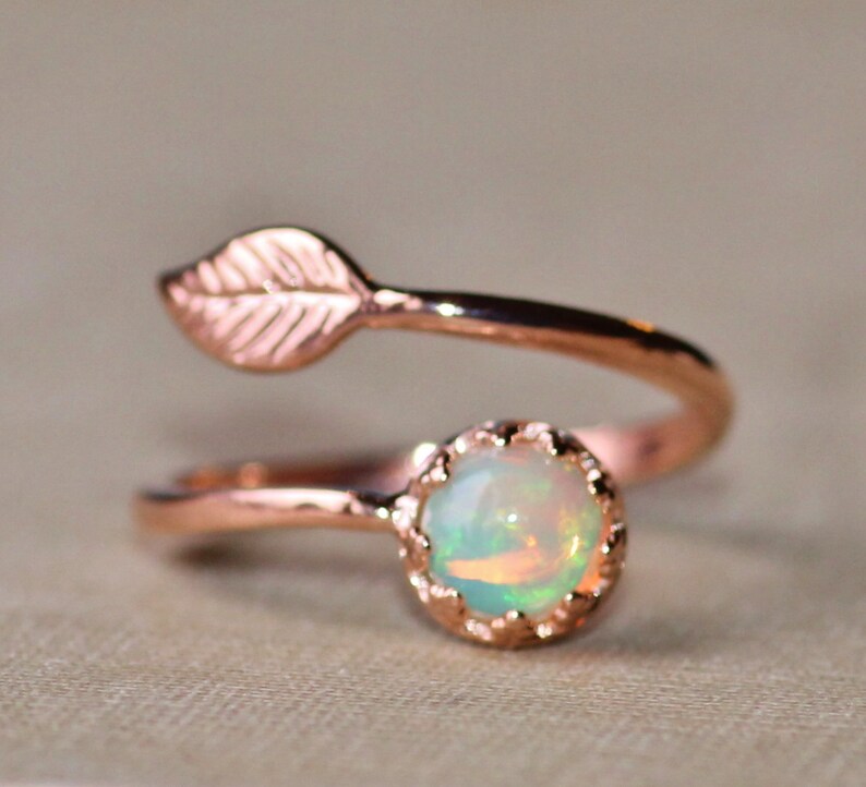 May include: A delicate rose gold ring with a small opal gemstone and a leaf design. The ring is a simple and elegant piece of jewelry.