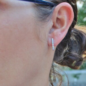 May include: A close-up of a person's ear with a small silver earring with a row of clear stones. The earring is a simple, elegant design.