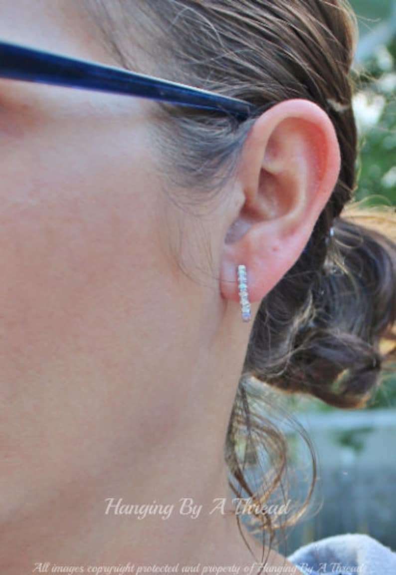May include: A close-up of a person's ear with a small silver earring with a row of clear stones. The earring is a simple, elegant design.