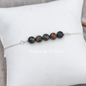 May include: A silver chain bracelet with six iridescent black beads. The beads have a green, orange, and red pattern.